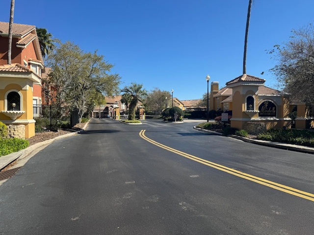 view of road featuring a gated entry, a residential view, curbs, and street lighting