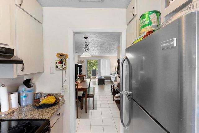 kitchen with light tile patterned floors, freestanding refrigerator, white cabinetry, a textured ceiling, and under cabinet range hood