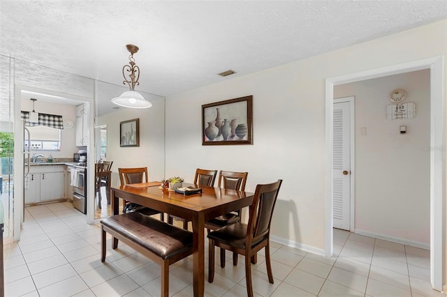 dining room with light tile patterned floors, a textured ceiling, visible vents, and baseboards