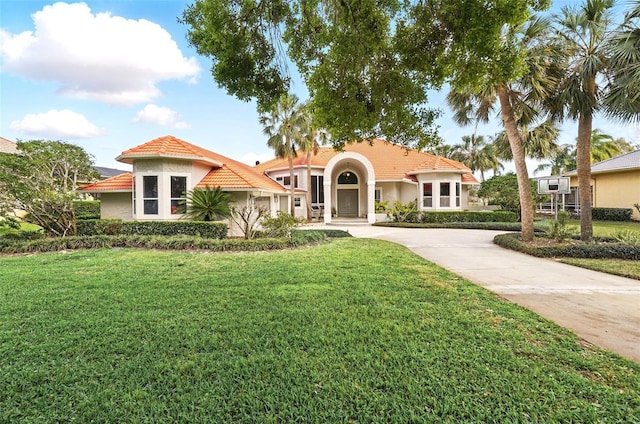 mediterranean / spanish-style home with concrete driveway, a front yard, a tiled roof, and stucco siding