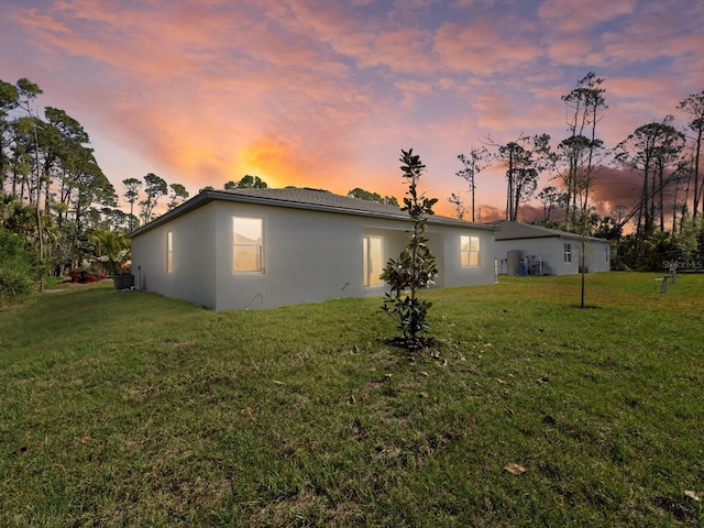 back of property with central air condition unit, a lawn, and stucco siding