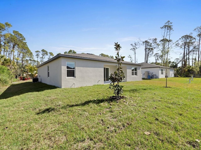 rear view of house featuring a lawn and stucco siding