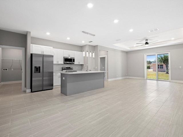 kitchen featuring stainless steel appliances, light countertops, open floor plan, white cabinets, and an island with sink