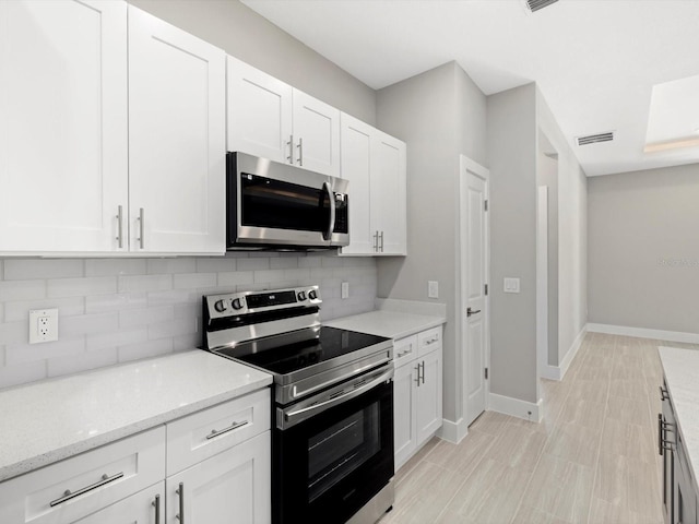 kitchen with light stone counters, backsplash, appliances with stainless steel finishes, white cabinetry, and baseboards