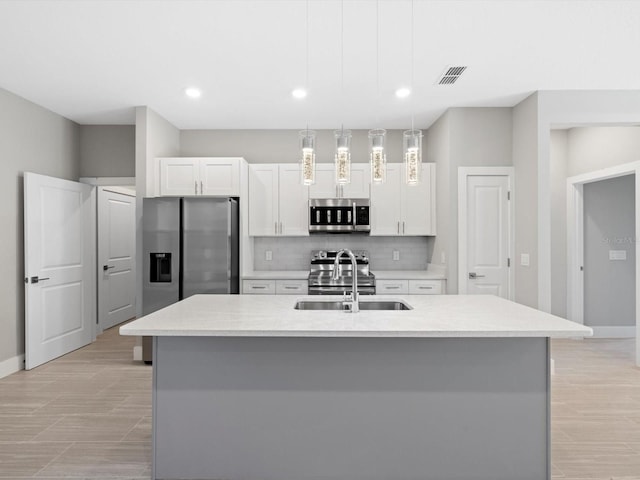 kitchen featuring stainless steel appliances, decorative backsplash, a kitchen island with sink, white cabinets, and a sink