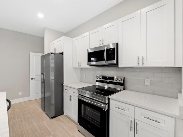 kitchen featuring tasteful backsplash, baseboards, white cabinets, appliances with stainless steel finishes, and light stone countertops