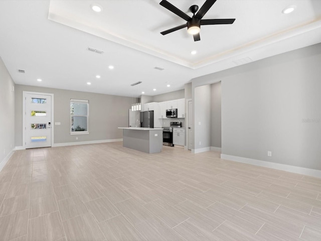 unfurnished living room with baseboards, visible vents, ceiling fan, a tray ceiling, and recessed lighting