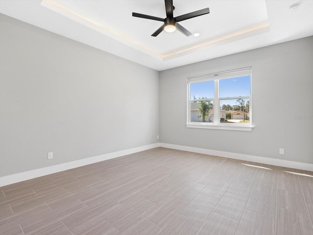 unfurnished room featuring a ceiling fan, a tray ceiling, wood finish floors, and baseboards