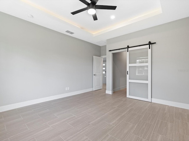 unfurnished bedroom featuring a tray ceiling, visible vents, baseboards, and a barn door