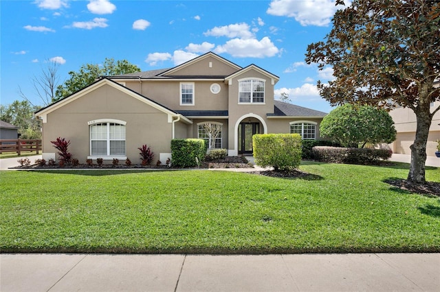 traditional-style house featuring fence, a front lawn, and stucco siding