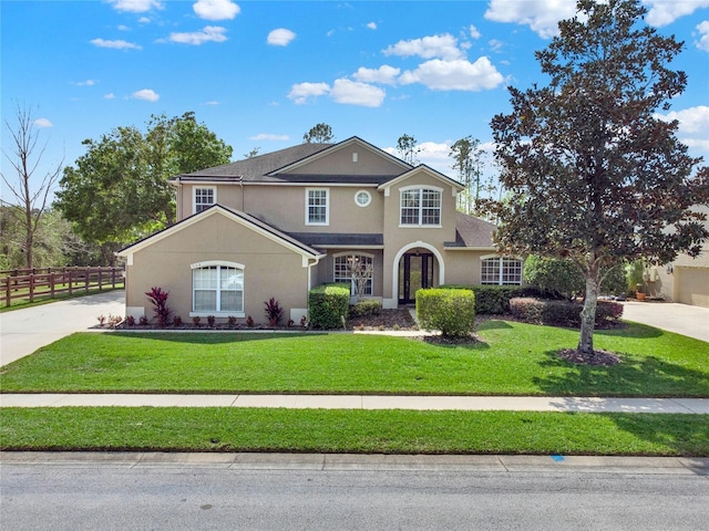 traditional home with driveway, a front yard, fence, and stucco siding