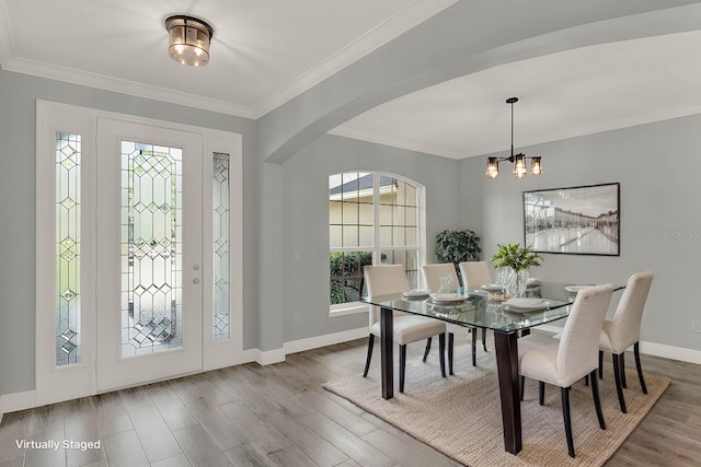 dining area with baseboards, arched walkways, wood finished floors, an inviting chandelier, and crown molding