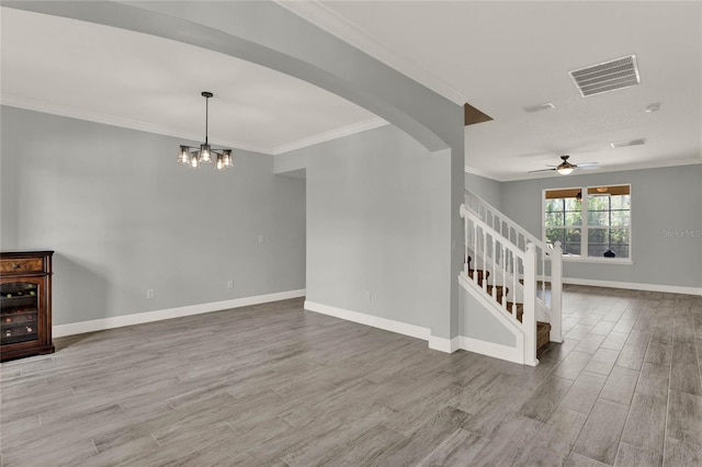 empty room featuring wood finished floors, visible vents, baseboards, stairs, and crown molding