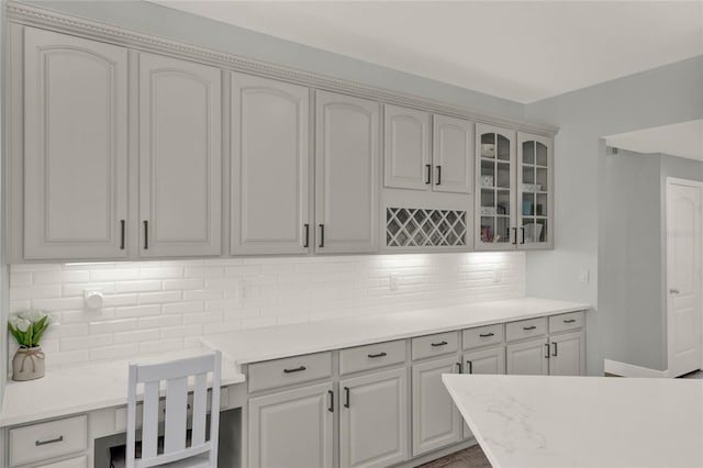 kitchen with light countertops, built in desk, backsplash, and glass insert cabinets