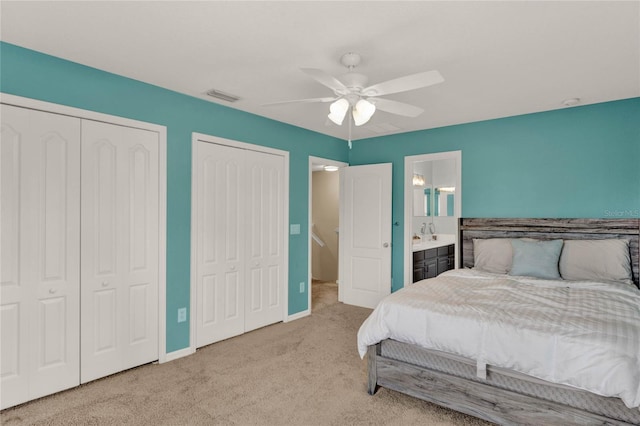 carpeted bedroom featuring multiple closets, visible vents, ensuite bathroom, ceiling fan, and baseboards