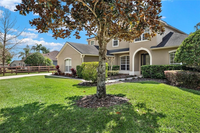 traditional-style house with a shingled roof, fence, a front lawn, and stucco siding