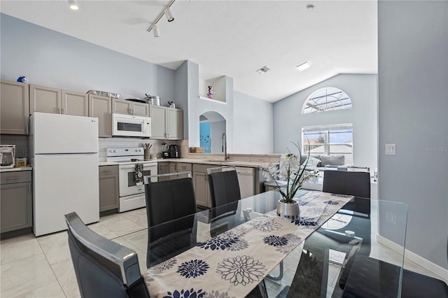 dining space with baseboards, visible vents, high vaulted ceiling, arched walkways, and rail lighting