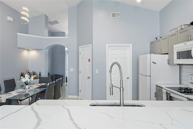 kitchen featuring visible vents, gray cabinetry, a sink, white appliances, and arched walkways