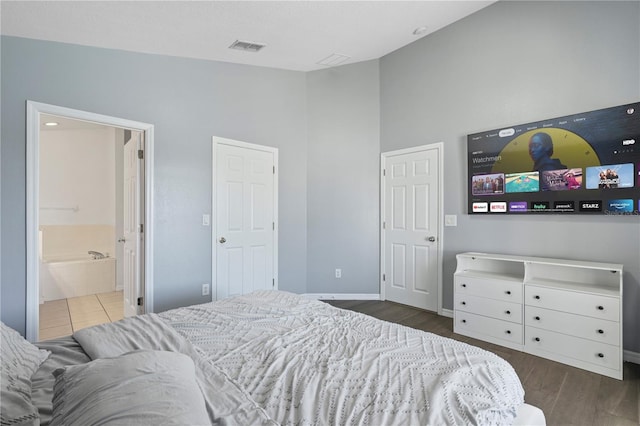 bedroom with visible vents, baseboards, lofted ceiling, ensuite bathroom, and wood finished floors