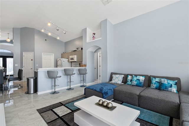 living area featuring visible vents, high vaulted ceiling, track lighting, arched walkways, and baseboards