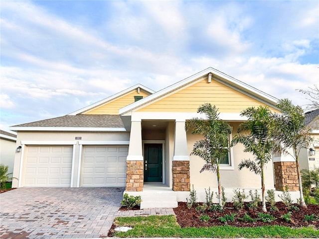 view of front of house featuring a garage, stone siding, roof with shingles, decorative driveway, and stucco siding