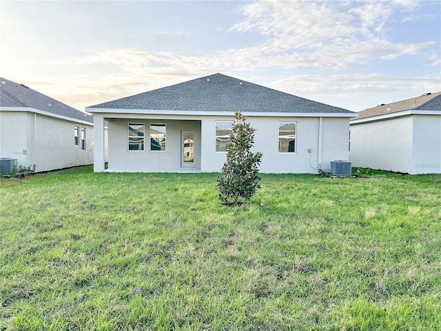 back of house featuring a yard, central AC unit, a shingled roof, and stucco siding