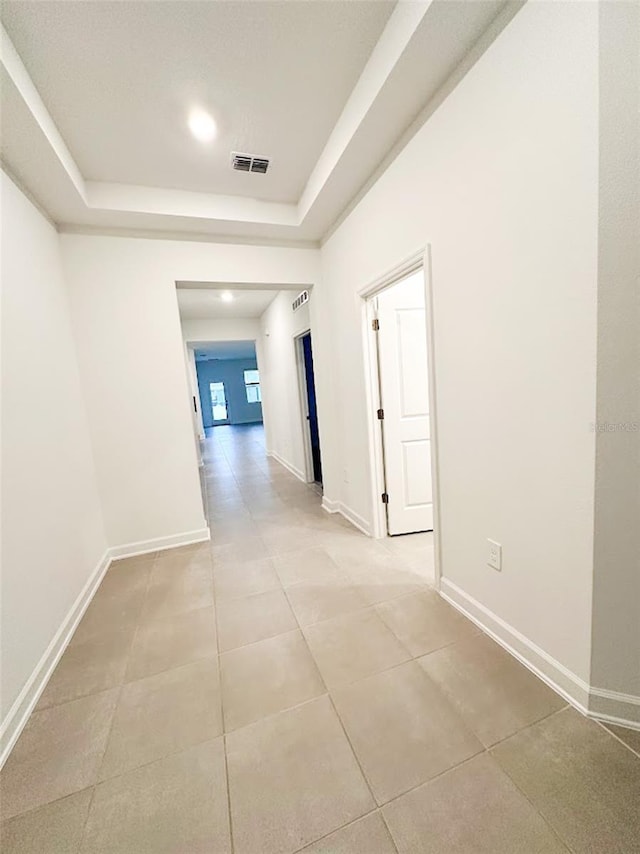 corridor with light tile patterned floors, a tray ceiling, visible vents, and baseboards