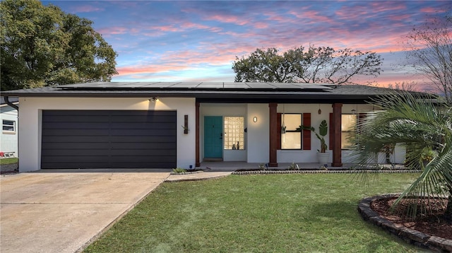 view of front of property with solar panels, stucco siding, a front yard, a garage, and driveway