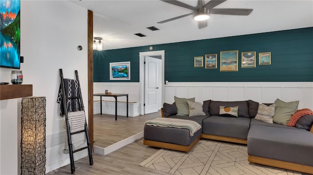 living room with a wainscoted wall, light wood finished floors, visible vents, and a ceiling fan