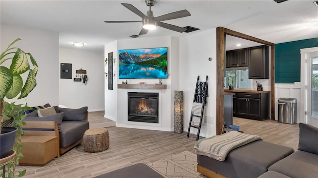 living room featuring a glass covered fireplace, visible vents, ceiling fan, and light wood finished floors