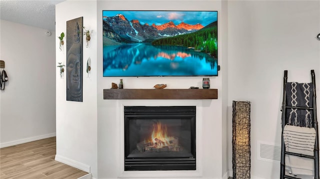 interior details with a textured ceiling, a glass covered fireplace, wood finished floors, and baseboards