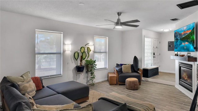 living area featuring a glass covered fireplace, baseboards, visible vents, and light wood finished floors