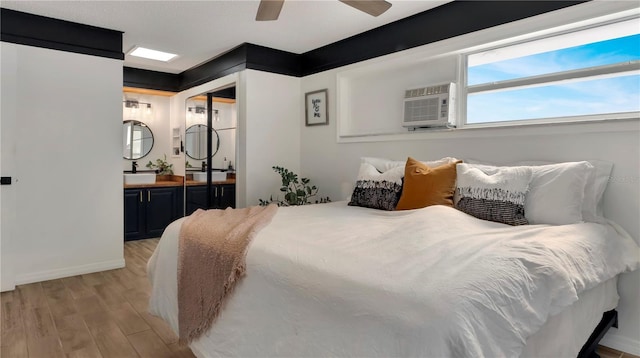 bedroom featuring light wood finished floors, baseboards, a ceiling fan, a wall unit AC, and a sink