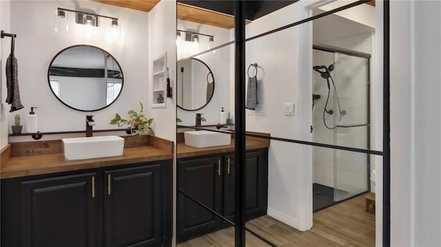 full bath featuring a stall shower, double vanity, a sink, and wood finished floors