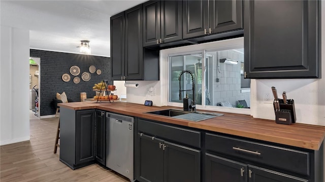 kitchen featuring wooden counters, light wood-style flooring, stainless steel dishwasher, a sink, and brick wall