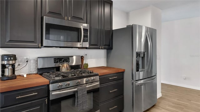 kitchen with stainless steel appliances, light wood-style floors, wooden counters, and baseboards