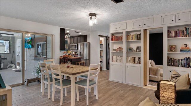 dining area featuring light wood-type flooring, visible vents, a textured ceiling, and a barn door