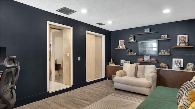 living room featuring recessed lighting, visible vents, a textured ceiling, and wood finished floors