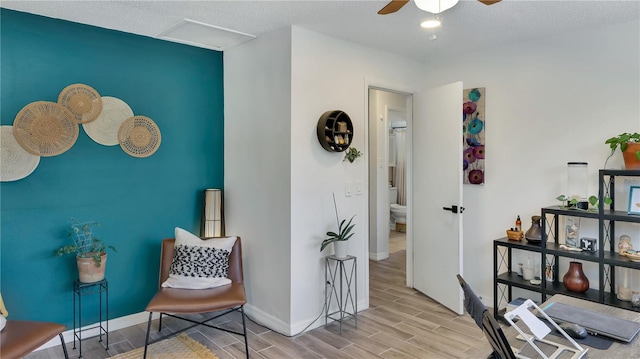 living area with wood finish floors, attic access, a ceiling fan, a textured ceiling, and baseboards