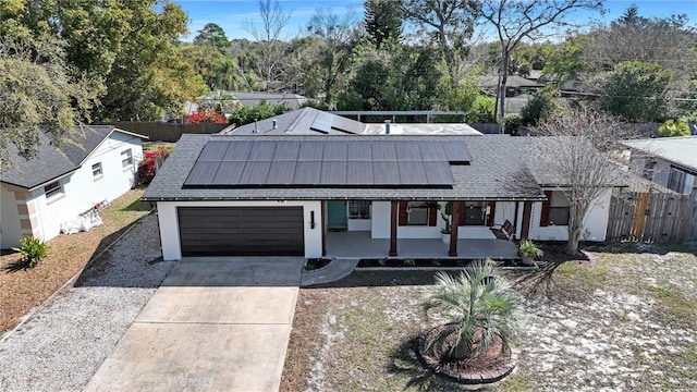 view of front facade featuring driveway, a shingled roof, solar panels, fence, and a porch