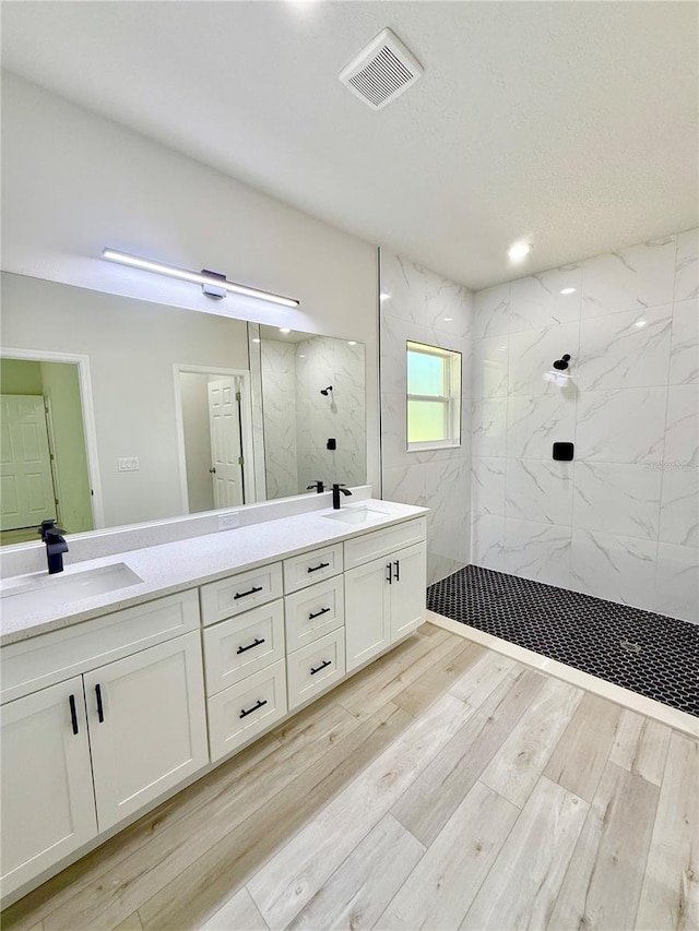 full bath with wood finished floors, visible vents, a marble finish shower, and a sink