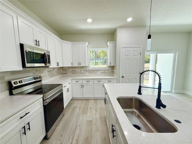 kitchen featuring a sink, decorative light fixtures, backsplash, white cabinetry, and stainless steel appliances