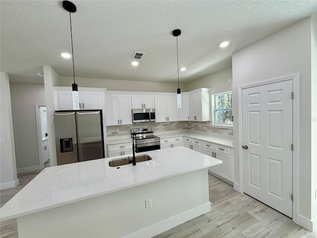 kitchen featuring visible vents, a kitchen island with sink, a sink, backsplash, and stainless steel appliances