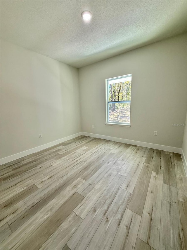 spare room featuring baseboards, light wood-style floors, and a textured ceiling