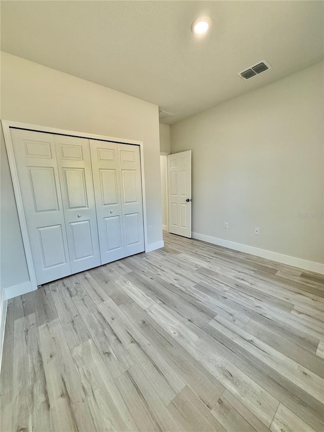 unfurnished bedroom featuring light wood finished floors, visible vents, a closet, and baseboards