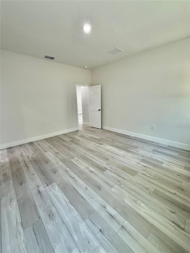 spare room with visible vents, baseboards, a textured ceiling, and light wood finished floors