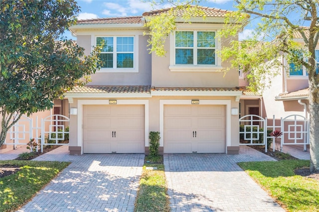 view of property featuring a garage, a tiled roof, decorative driveway, and stucco siding