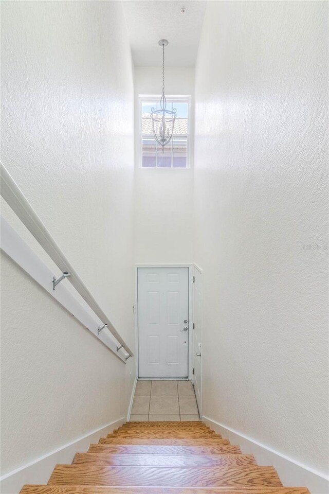 staircase with a towering ceiling, an inviting chandelier, tile patterned flooring, and baseboards