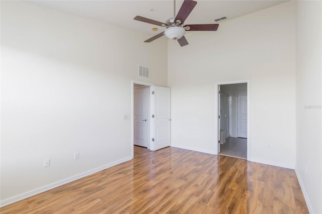 unfurnished bedroom with a towering ceiling, baseboards, visible vents, and wood finished floors