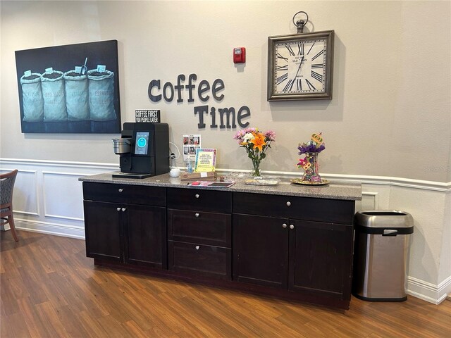 bar with dark wood-style floors, a decorative wall, and wainscoting